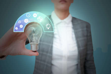 Lady in suit holding light bulb representing innovative thinking symbolizing futuristic technology. Woman presenting electrical lamp displays sucessful creative thinking.の写真素材