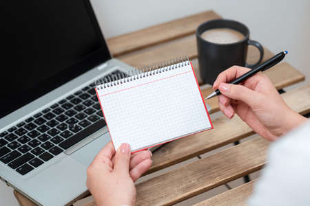 Businesswoman Holding Pen And Notepad With Important Message On Table With Lap Top And Coffee. Woman...