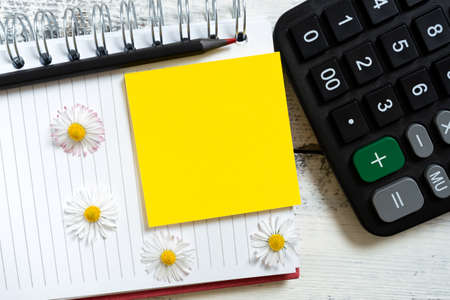 Sticky Note With Important Message Over Notebook With Pencil And Flowers On Desk With Calculator. Memo With Crutial Information Over Notepad On Table.の写真素材