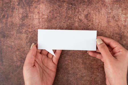 Hands Of Woman Holding Speech Bubble Of Empty Paper Over Wooden Background. Businesswoman With Blank Sheet And Representing Thoughts And Business Opinions.の写真素材