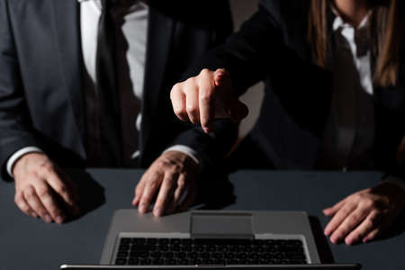 Sitting Man On Desk With Lap Top And Woman Pointing With One Finger On Important Messages. Businesswoman Presenting Crutial Informations With One Hand.の写真素材