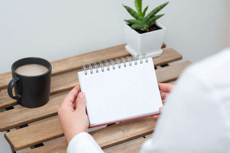 Woman Holding Notebook With Important Message On Table With Coffee And Plant. Businesswoman Presenting Crutial Information On Desk With Cup And Flower.の写真素材