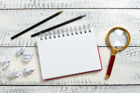 Notebook With Important Message On Floor With Paper Wraps, Magnifier And Pencils Around. Notepad...