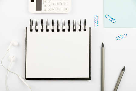 Notebook With Important Message On Desk With Pens, Calculator, Headphones And Paperclips. Notepad With Crutial Information On Table With Pencils And Colored Clips.の写真素材