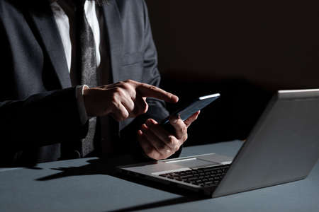 Businessman Holding Mobile Phone In Hand And Pointing With One Finger On It On Desk With Lap Top....