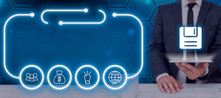 Businessman Holding A Tablet With A Floppy Disk And Glowing Digital Symbols In Futuristic Frame. Man...