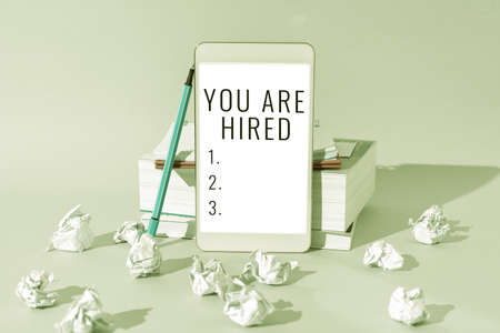 Handwriting text You Are Hired. Business showcase Recruitment being selected for a job the right candidate Important Messages Presented On Mobile Phone Leaning On Books And Notebook.の写真素材