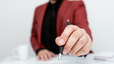 Male model in Red suit sitting at white table And Pointing With Pen On Important Message. Gentleman Showing Critical Announcement. Coffee cup on deck.の写真素材