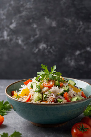 Freshly made rice salad with colorful vegetables served in a bowl against a dark background perfect for healthy food promotions.の素材