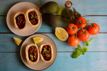 Traditional dish - Mexican tacos with ingredients beans and vegetables on the plate on a blue wooden background, top view. Lots of space for text and design.の写真素材