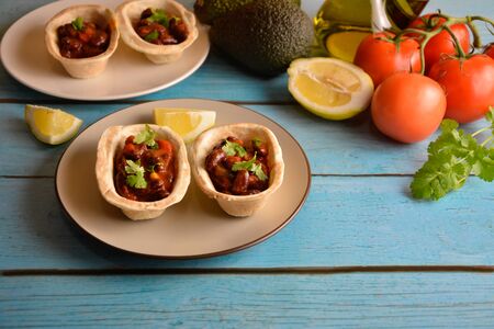 Traditional dish - Mexican tacos with ingredients beans and vegetables on the plate on a blue wooden background.の写真素材
