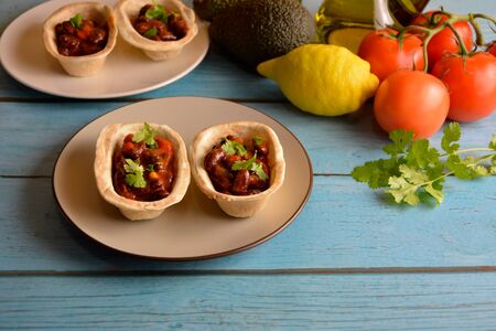 Traditional dish - Mexican tacos with ingredients beans and vegetables on the plate on a blue wooden background.の写真素材