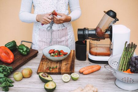 Young woman preparing organic juice with cold pressed extractor machine - Girl making smoothie with vegetables and fruit - Healthy lifestyle nutrition during isolation quarantine - Focus on handsの写真素材