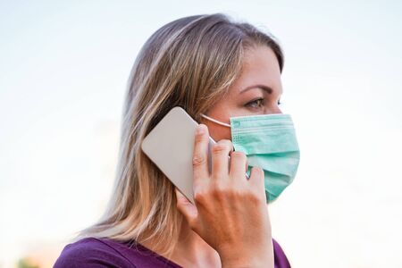 Young woman talking with mobile phone outdoor wearing face mask and latex gloves for Covid-19 virus prevention - Girl speaking with smartphone outside during quarantine isolation - Focus on fingerの写真素材