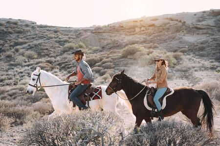 Young people riding horses doing excursion at sunset - Wild couple having fun in equestrian tour  - Training, culture, passion, healthy lifestyle, sport conceptの写真素材