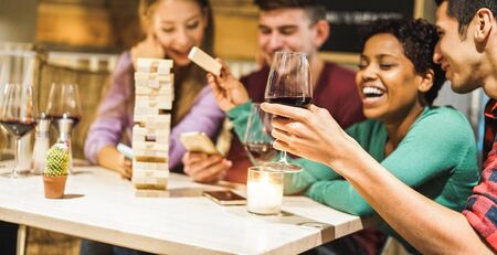 Young friends playing board games at home - Happy people having fun doing party in living room house at evening time - Fest during isolation quarantine - Focus on close-up hand wine glassの写真素材