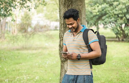 Young indian man using smartphone app in university campis - Happy asian guy having fun watching videos on mobile cell phone - Technology and millennial generation concept - Focus on his faceの写真素材