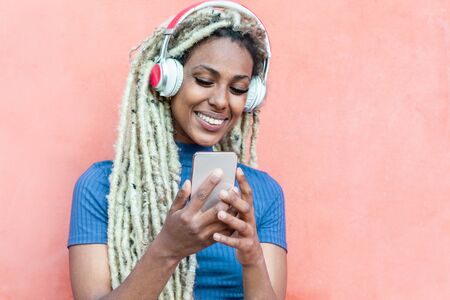 Happy african girl watching videos and listening music with mobile phone app - Young person having fun with new technology trends - Focus on faceの写真素材