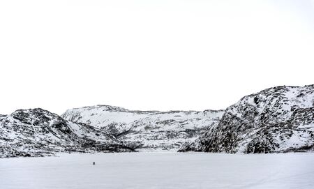 Walking on white. Two people Nordic walking on a frozen lake or field surrounded by snow covered hills under a white skyの写真素材