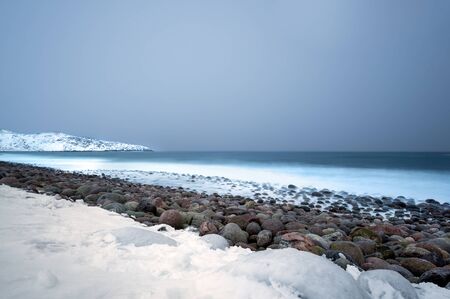 Long exposure of the surf breaking over stone boulders on a snow covered beachの写真素材