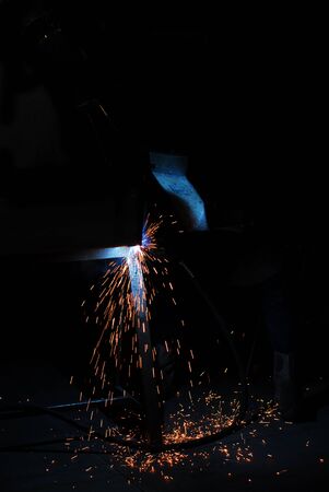 Welder illuminated only by sparks and wearing a welding mask against a complete black background