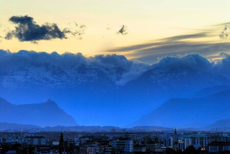 View of Turin (Torino) Italy at sunset looking toward Susa Valley with the backdrop of the Italian Alps and the Sacra di San Michele Church silhouettedの写真素材