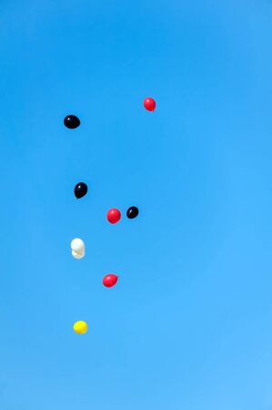 Colored balloons fly away in crystal clear light blue sky. Red, yellow, black and white balloons.の写真素材