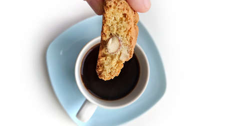 Traditional Italian Cantuccino (or Cantuccio) almond biscuit (cookie) ready to be dunked in an espresso coffee cup on a light blue coaster, isolated on white backgroundの写真素材