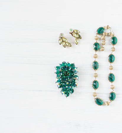 Woman's Jewellery. Vintage jewelry background. Beautiful bright rhinestone emerald brooch, necklace and earrings on white. Flat lay, top viewの写真素材