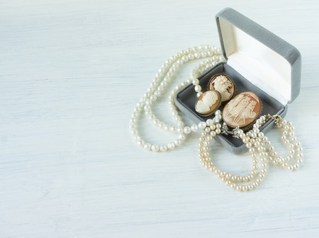 Womans Jewelry. Vintage jewelry background. Beautiful pearl necklace, bracelet and old cameos in a gift box on white wood. Flat lay, top viewの写真素材