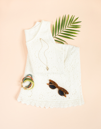 Summer fashion, summer outfit on cream background. White lace dress, retro sunglasses, wood bracelet. Flat lay, top viewの写真素材