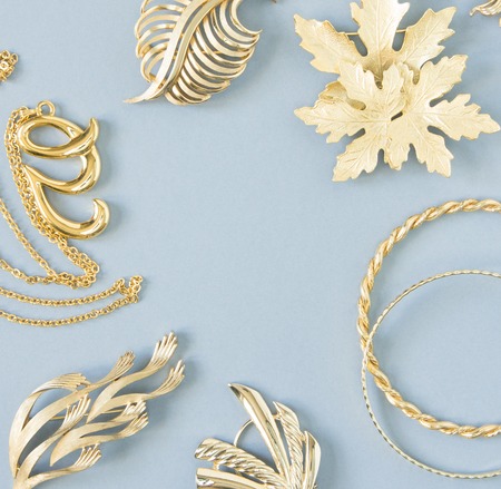 Womans Jewelry. Vintage jewelry background. Beautiful gold tone brooches, braceletes, necklaces and earrings on blue background. Flat lay, top view.の写真素材