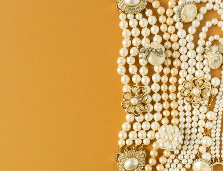 Pearls background. Womans Jewelry. Vintage jewelry background. Beautiful gold tone and pearls brooches, braceletes, necklaces and earrings on mustard background. Flat lay, top view.の写真素材