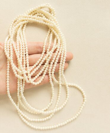 Woman's Jewelry. Vintage jewelry background. Beautiful pearl necklace on hand on cream background. Flat lay, closeupの写真素材