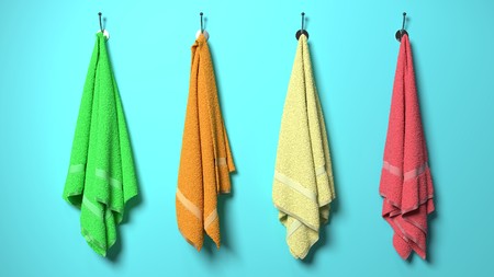Four soft cotton, fluffy,colorful, green, orange, yellow and red towels hanging on a sea light blue wall, symbolize health, spa and massage, happiness, beach and vacationの写真素材