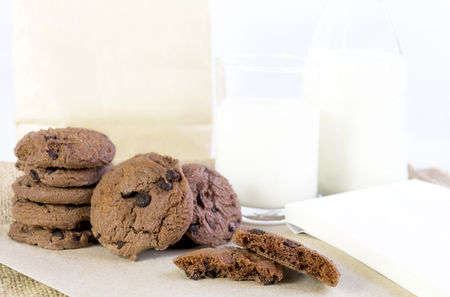 Chocolate chip cookies on brown paper and sack cloth with glass of milk and paper bag on white background. With copy space for textの写真素材