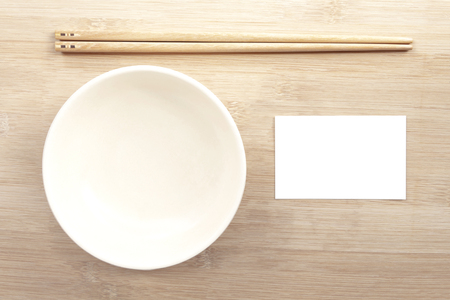 Ceramic bowl with chopsticks and paper mock up white card on wooden table background with copy space for text. Creative layout with food concept.の写真素材