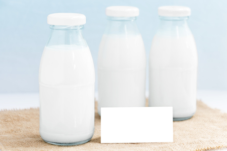 Three glass bottle of milk on the sackcloth and paper white mock up with blue background. with copy space for text.の写真素材