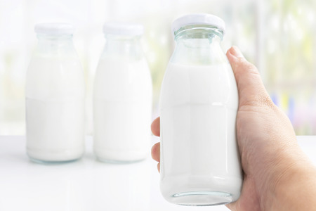 Woman's hand holding a bottle glass of milk isolated on white table background for food and healthy concept.の写真素材