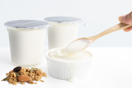 Hand's woman holding wooden spoon with healthy flavored yogurt in plastic cup and ceramic bowl with cereal and  isolated on the white background. With copy space for your text.の写真素材