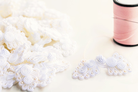 Button knot chinese : A lot of traditional chinese white knot buttons with thread and sewing needle on the white background.の写真素材