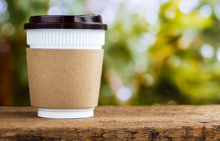 Paper coffee cup or disposable cup on the wooden table on natural morning background with copy space for your text and logo.の写真素材