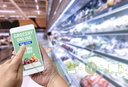 Online grocery shopping concept: Woman hand holding smart phone for ordering food onscreen with icon media on supermarket background. Business and technology for lifestyle in city.の写真素材