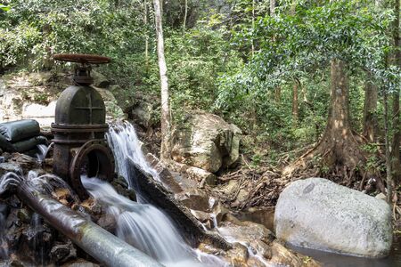 The water flowing from the steel drain into the brook of the waterfall in the tropical forest.の写真素材