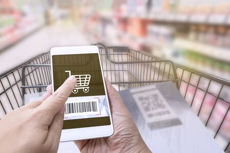 Online order grocery shopping on touch screen concept. Woman hand holding smart phone and scanning barcode for ordering ingredients food which delivery service at home for cooking.の写真素材