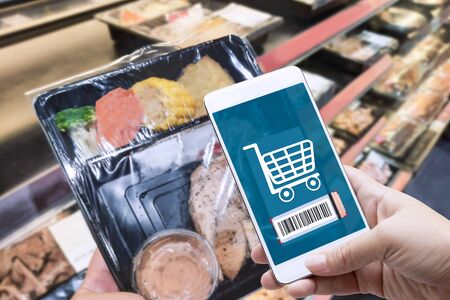 Online order grocery shopping on touch screen for ready meal food concept. Woman hand holding smart phone and scanning barcode for delivery service or take out at home. Business and technology.の写真素材