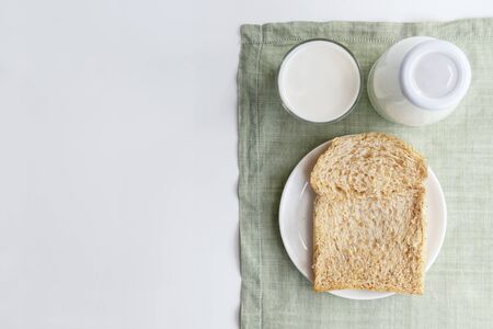 A bottle of milk and glass of milk with sliced bread on dish on green cloth on white background. Healthy food for breakfast concept with copy space for text.の写真素材