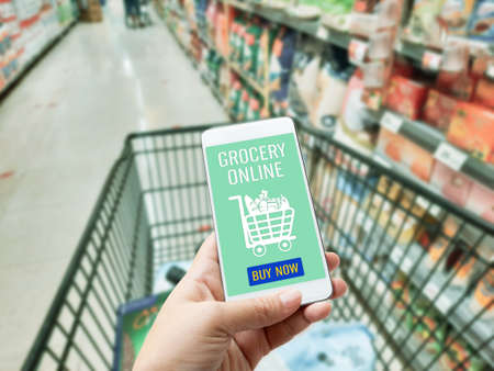 Online order grocery shopping on touch screen concept. Woman hand holding smart phone for ordering food delivery ingredients service at home for cooking. Business and technology for lifestyle in city.の写真素材