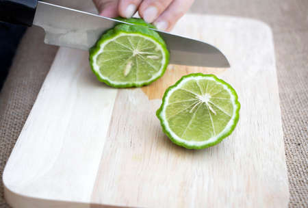 Women holding knife cutting slices raw Bergamot fruit fresh on wooden cutting board on sackcloth background. Bergamot material of essential oils for beauty and cooking food ingredient healthy.の写真素材