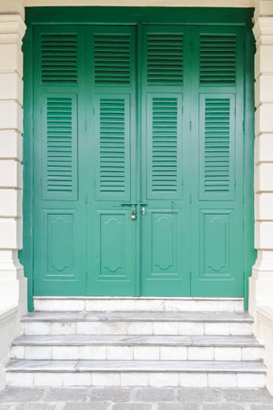 Vintage green wooden door made of plank with window shutter and  locked padlock on the cement wall yellow color with style traditional for background and texture.の写真素材
